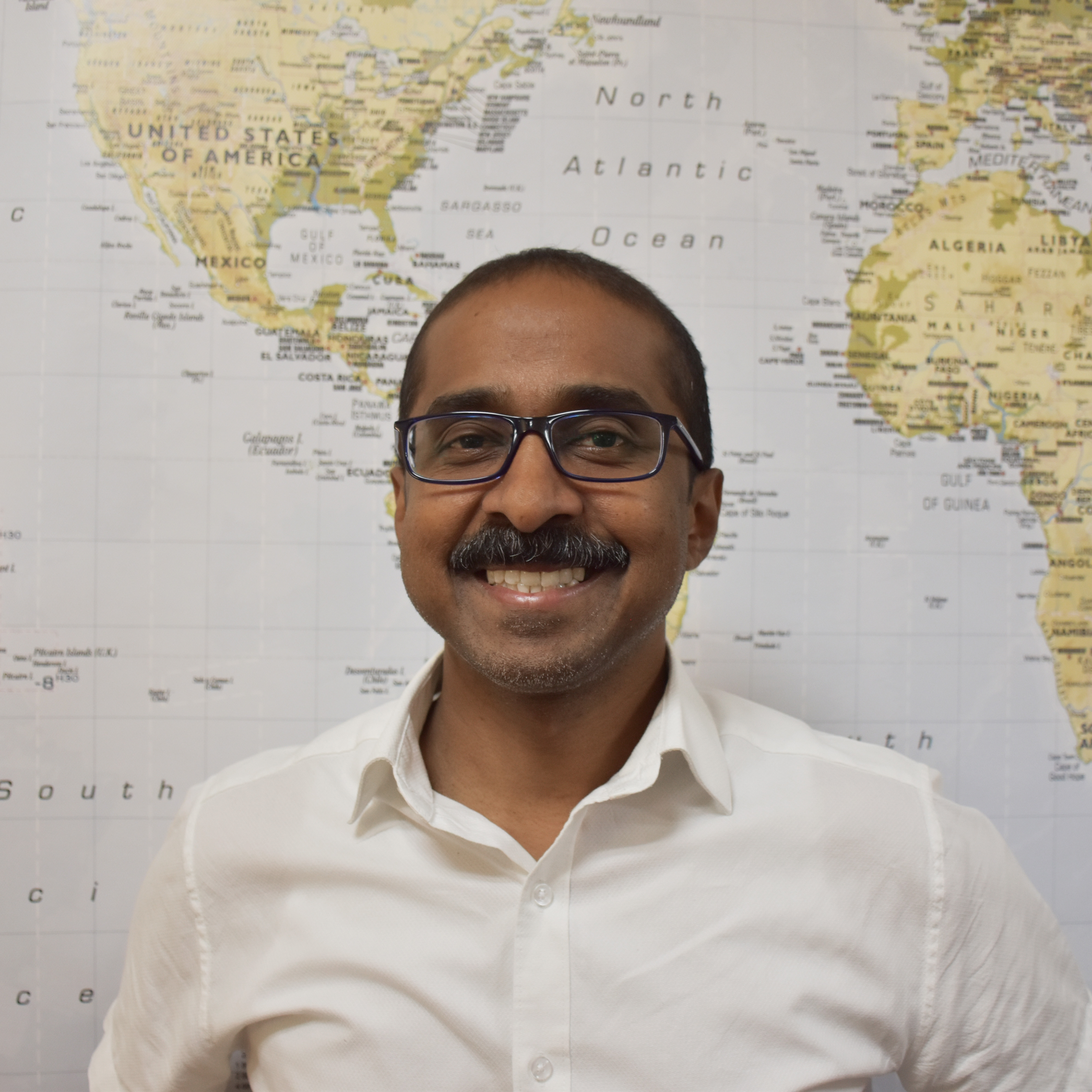 Jay Arasan, Associate Director, smiling in front of a global map